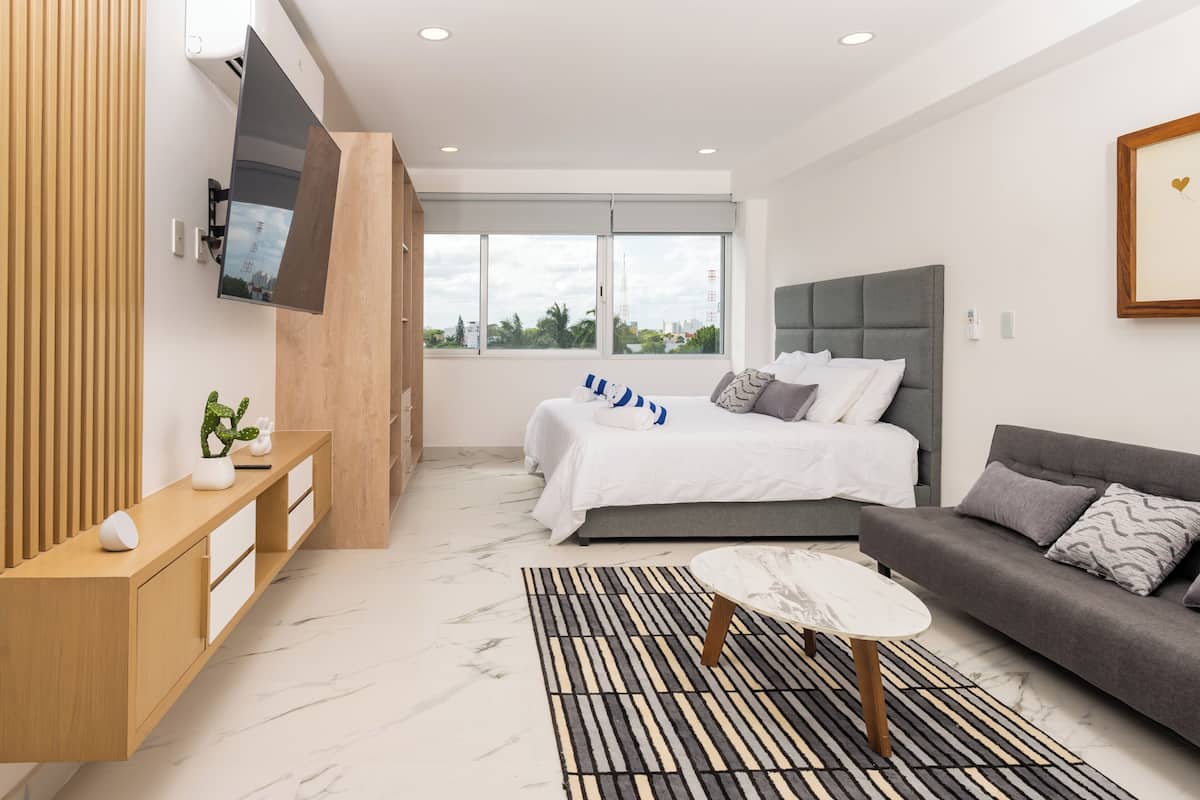 A modern bedroom with a bed, a sofa, a TV, and a console table.
