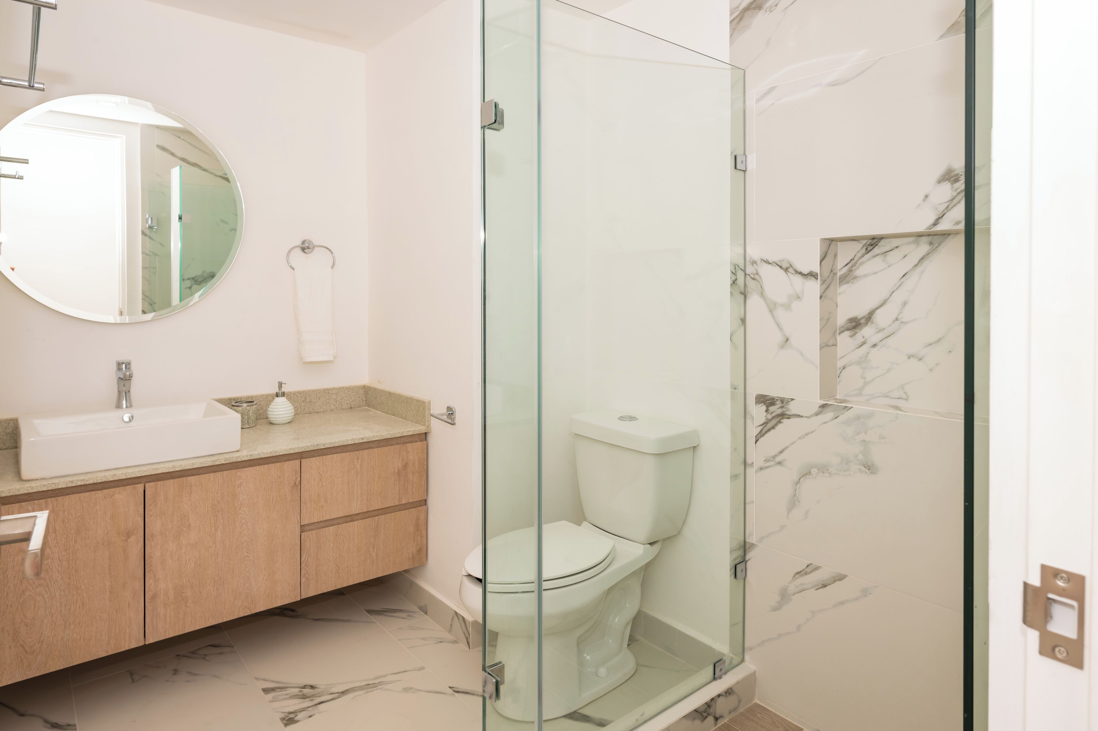 Un baño moderno con ducha acristalada, lavamanos con encimera de mármol y un inodoro.