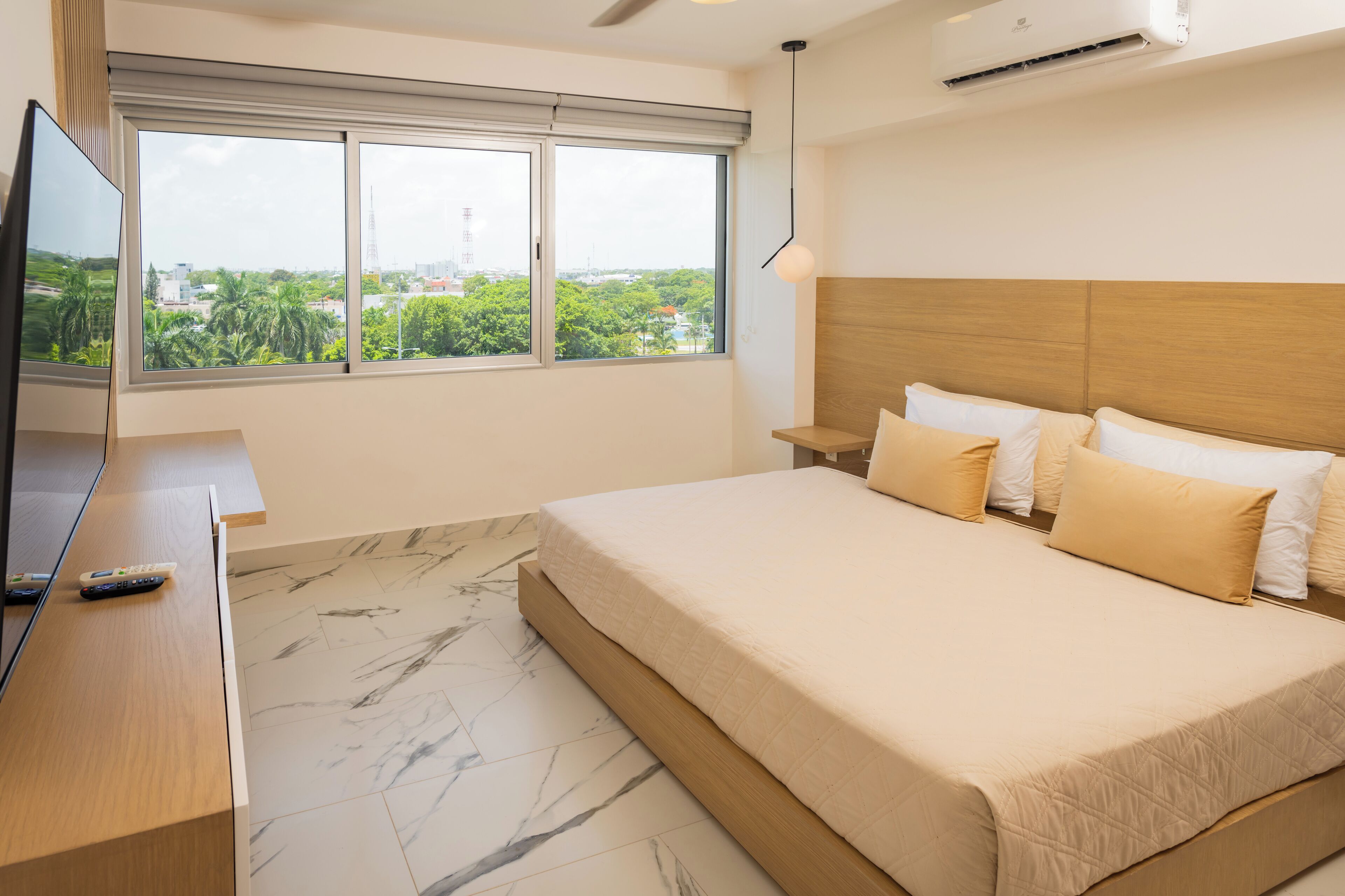 A modern hotel room with a large bed, a TV, and a window with a city view.