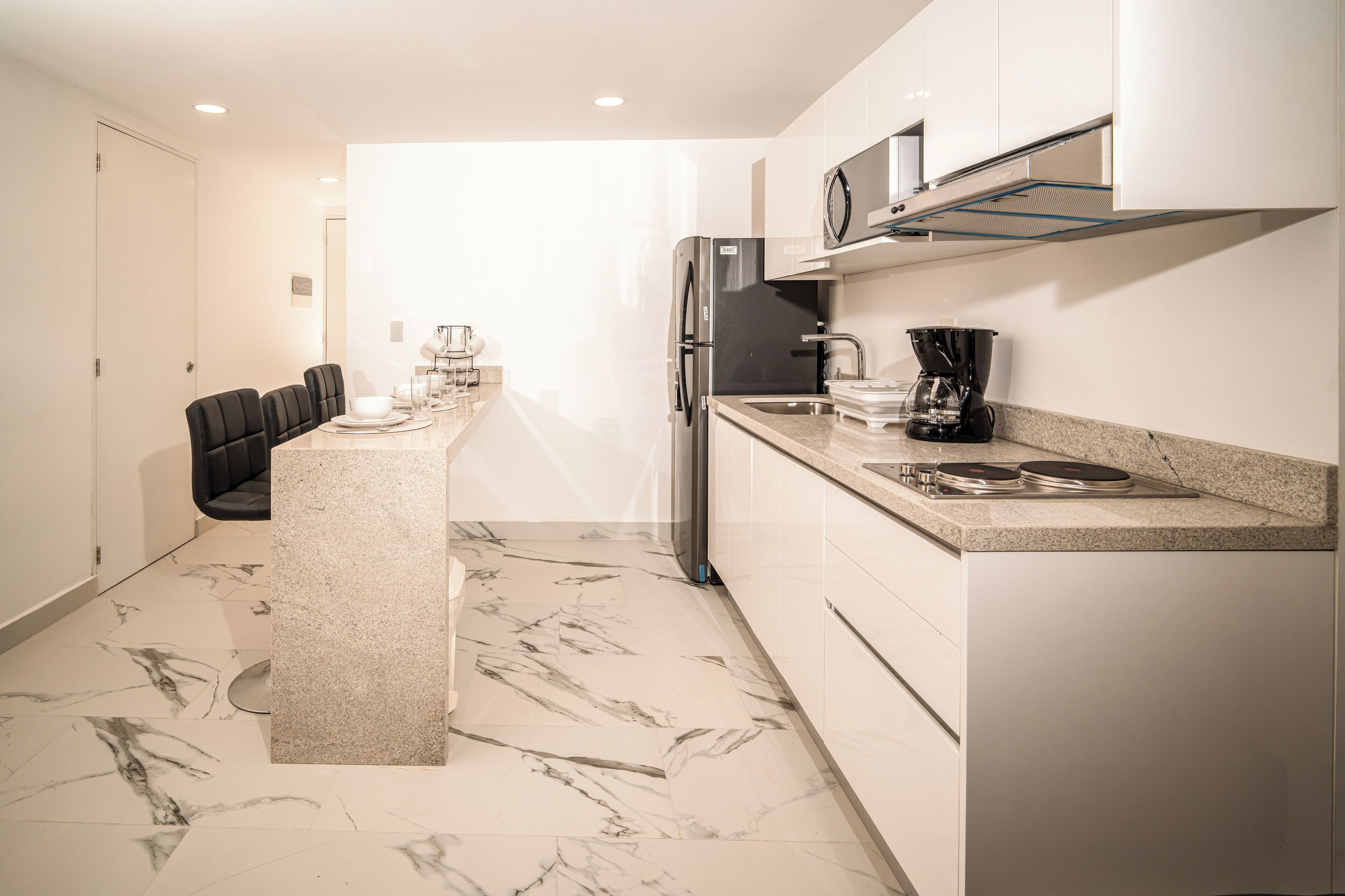 A modern kitchen with a marble floor, a refrigerator, a coffee maker, and a dining area with chairs and a table.