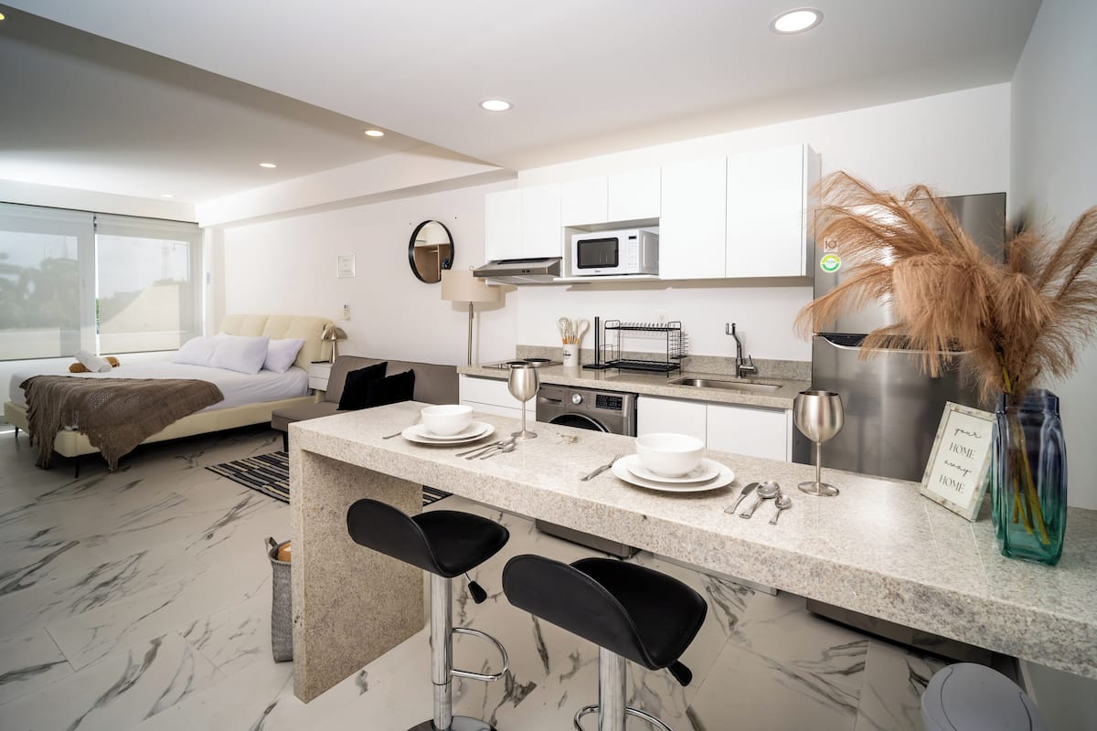 A modern kitchen with a central island, bar stools, a microwave, and a refrigerator.