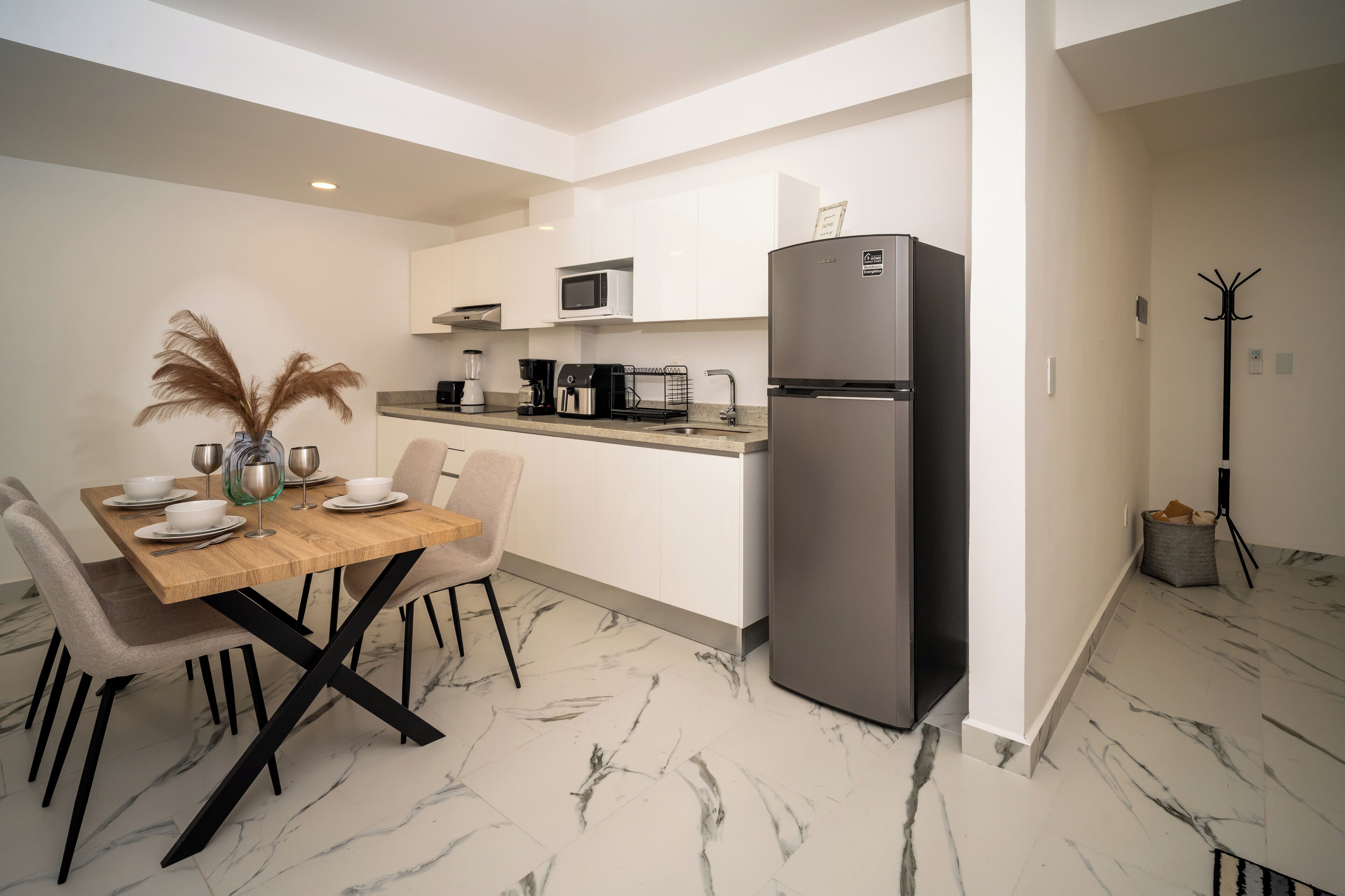 A modern kitchen with white cabinets, a black refrigerator, and a dining area with a wooden table and chairs.