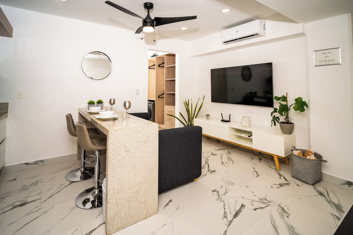 A modern kitchen with a marble countertop, bar stools, and a built-in TV.
