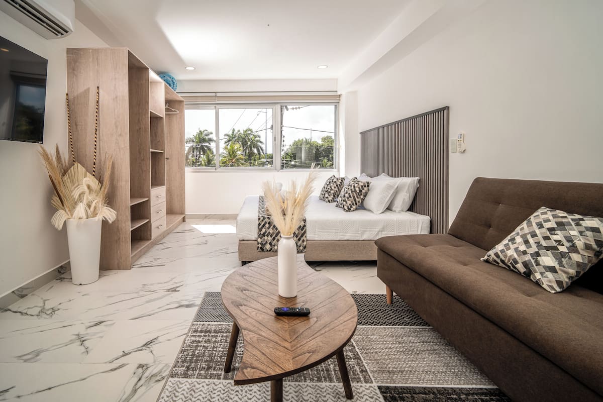 A modern living room with a sofa, a coffee table, a TV, and a large window with a view of palm trees.