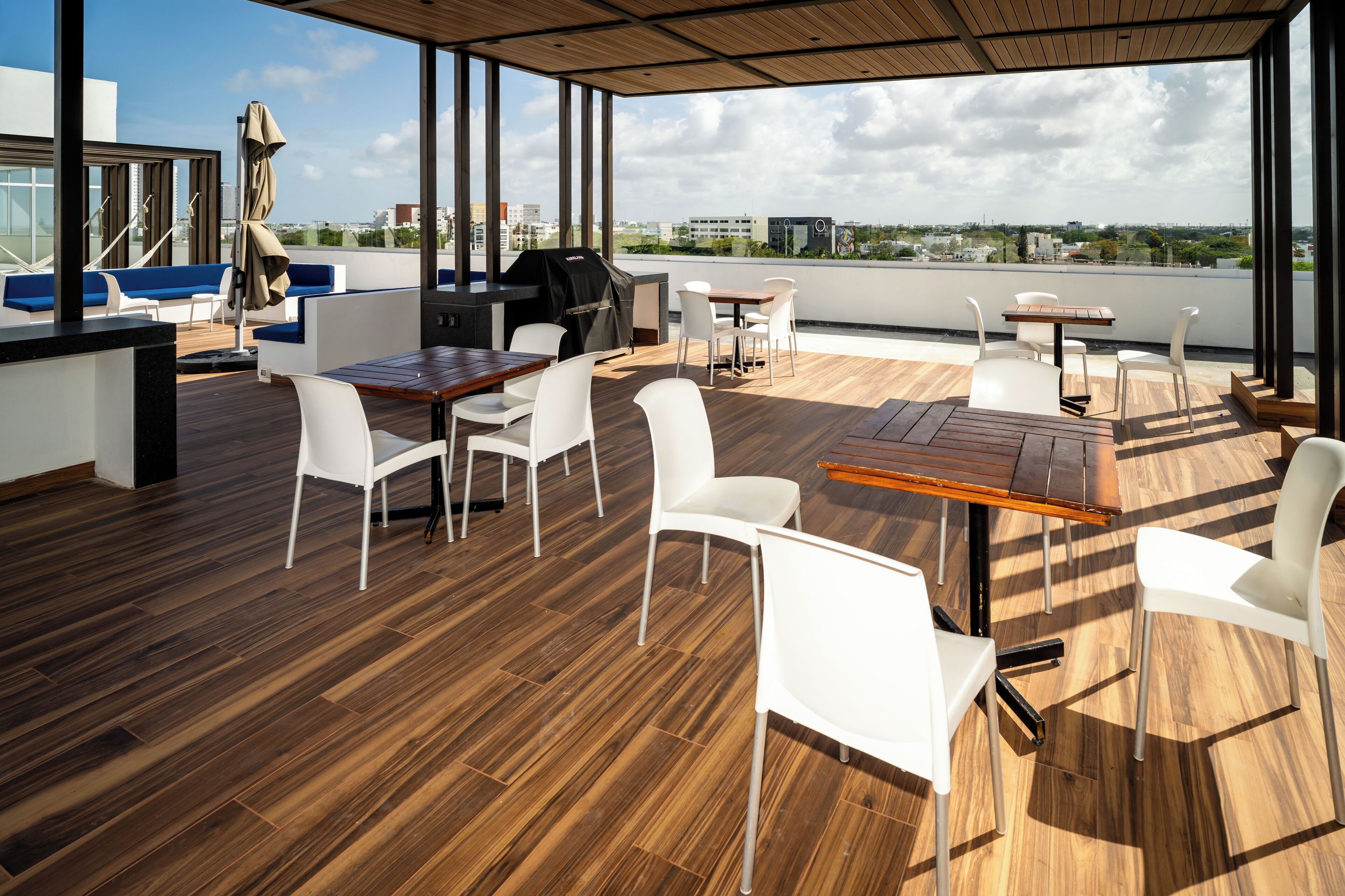 Eine Dachterrasse mit Holzboden, weißen Stühlen, einem Holztisch, einem Grill und Blick auf die Stadt.