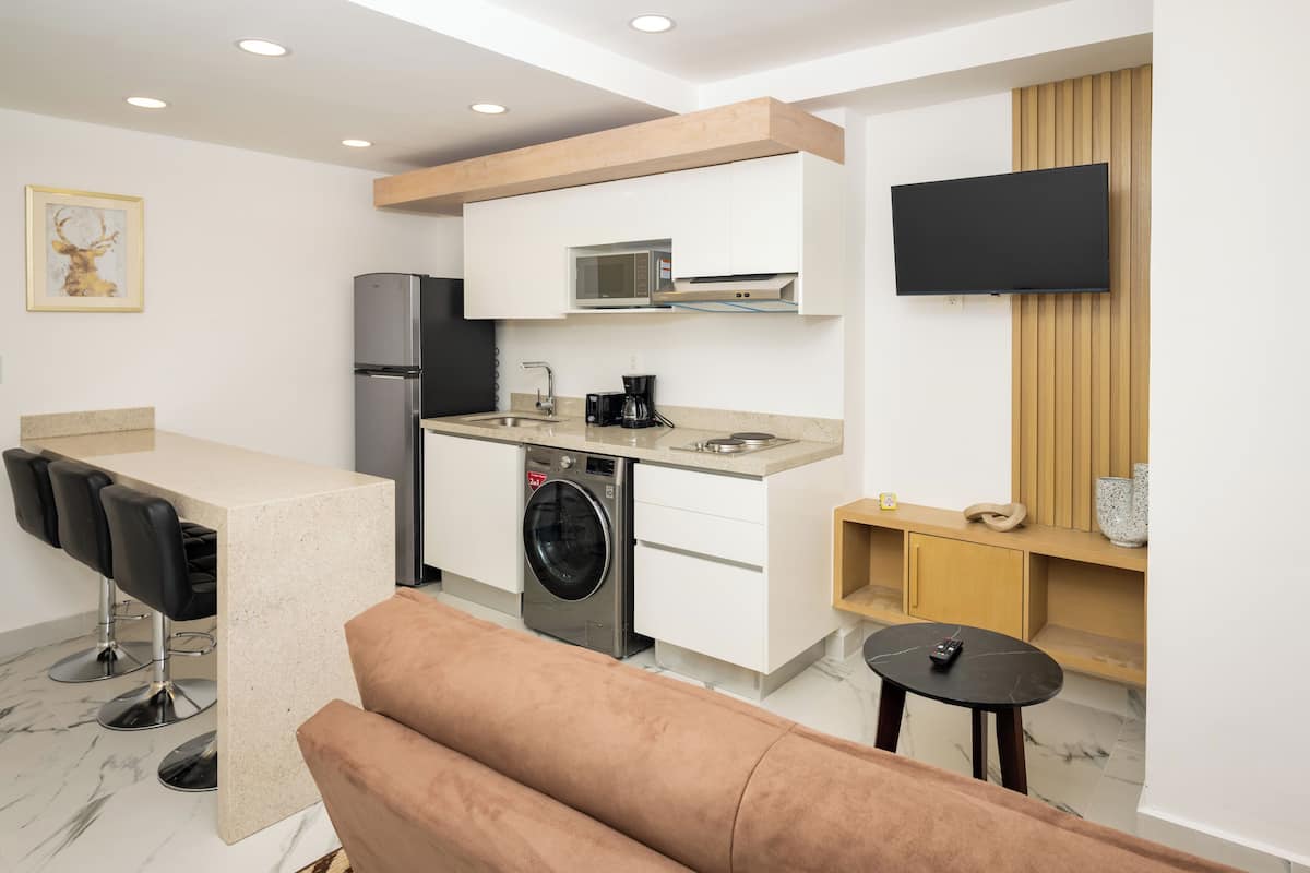 A compact kitchen with a microwave, refrigerator, and washing machine. There is a bar area with stools and a sofa in the living space.