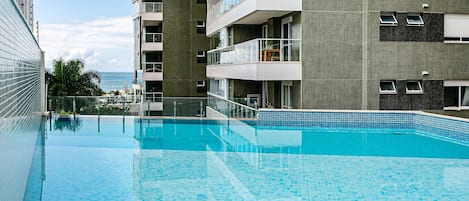 A swimming pool with a tiled edge, surrounded by multi-story buildings with balconies and windows.