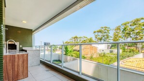Ein Balkon mit eingebautem Grill, Blick auf die nähere Umgebung und ein gefliester Boden.