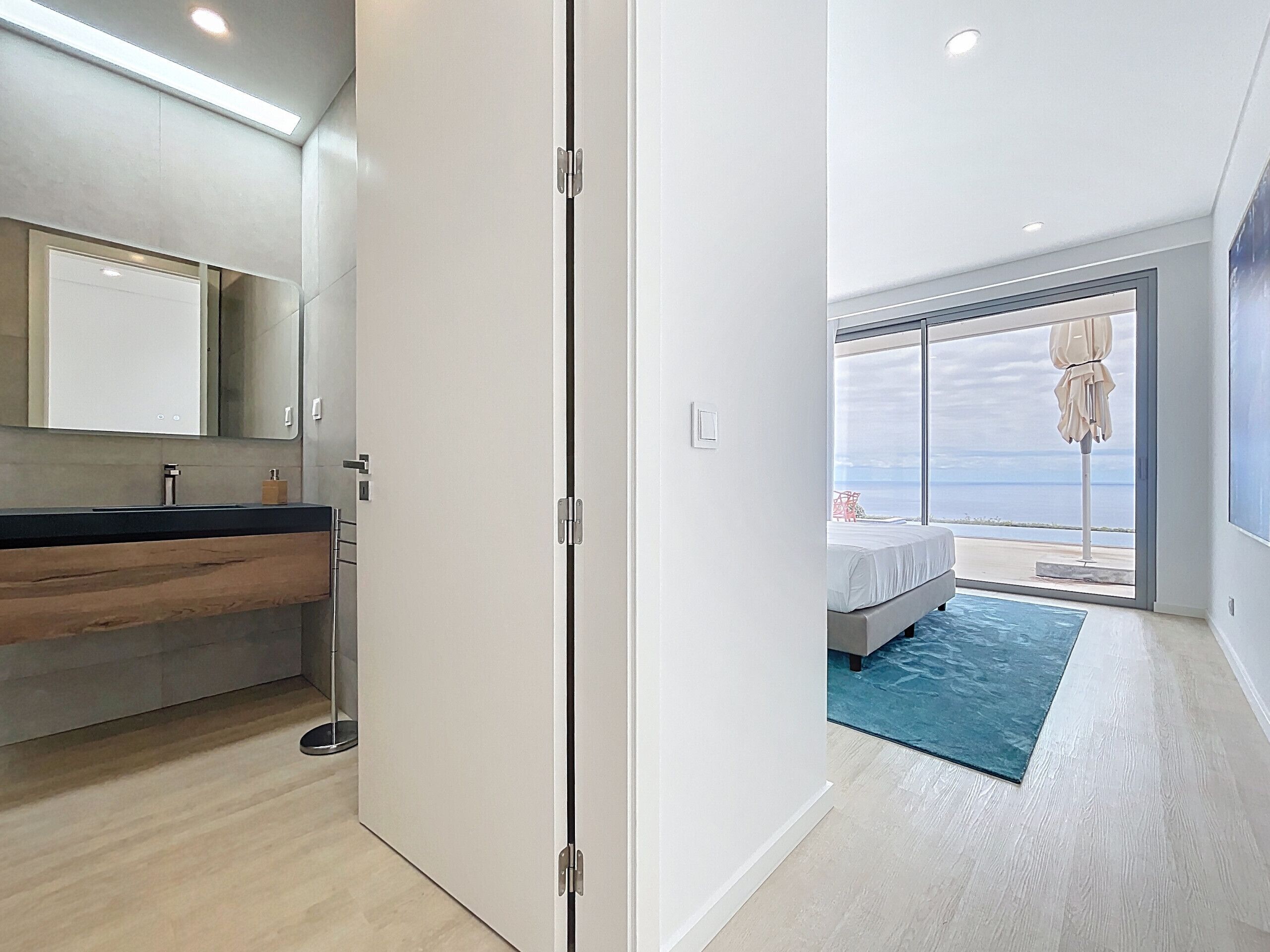 A modern bedroom with a large window, a bed, and a view of the sea.