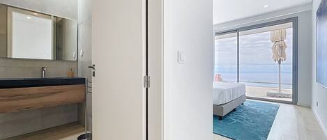 A modern bedroom with a large window, a bed, and a view of the sea.