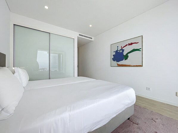 A modern hotel room with a large bed, a sliding glass door closet, and a colorful abstract painting on the wall. - Villa Alegria by Atlantic Holiday (Calheta)