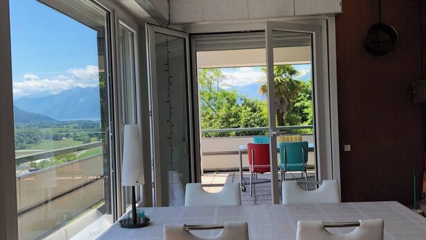 Un comedor con mesa y sillas, ventanas amplias con vistas a montañas y vegetación, y una puerta corrediza de vidrio que da a un espacio de estar al aire libre.