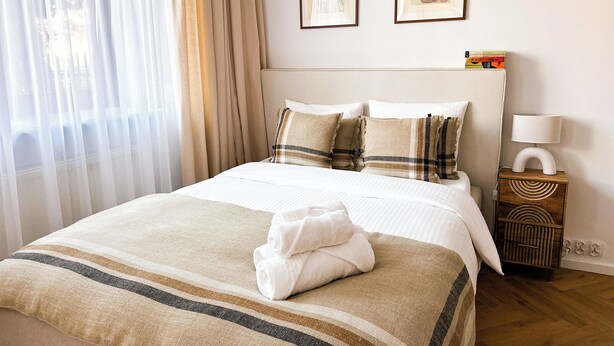 A neatly made bed with a striped blanket, a bedside table with a lamp, and two framed artworks on the wall.