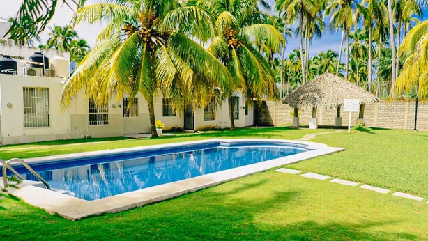 A swimming pool surrounded by a well-maintained lawn and palm trees. - 2 bedroom house with swimming pool in Ixtapa (San José Ixtapa)