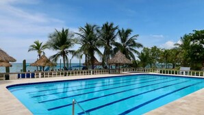 A swimming pool with clear blue water, surrounded by palm trees and a beach view.