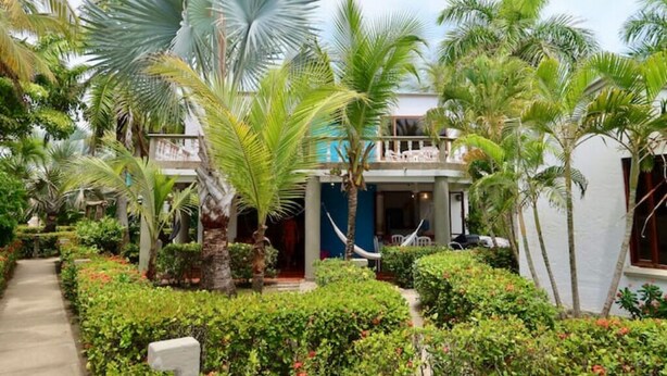 A tropical resort with a pool, palm trees, and a two-story building with a balcony.
