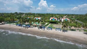 A beachside hotel with multiple buildings, a sandy beach, and palm trees.
