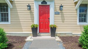 A beige house with a red door, two potted plants, and a number sign above the door. - Historic Home with Colonial Charm in Manchester (Manchester)