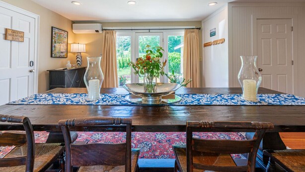 A dining room with a wooden table, four chairs, a vase with flowers, and a view of greenery outside. - Historic Home with Colonial Charm in Manchester (Manchester)