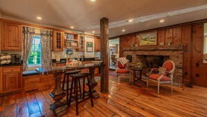 A rustic kitchen with wooden cabinets, a stone fireplace, and a dining area with red upholstered chairs. - Historic Home with Colonial Charm in Manchester (Manchester)