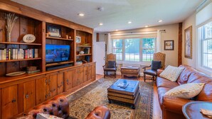 A cozy living room with a wooden entertainment center, leather sofa, and a large window offering a view of the outdoors. - Historic Home with Colonial Charm in Manchester (Manchester)