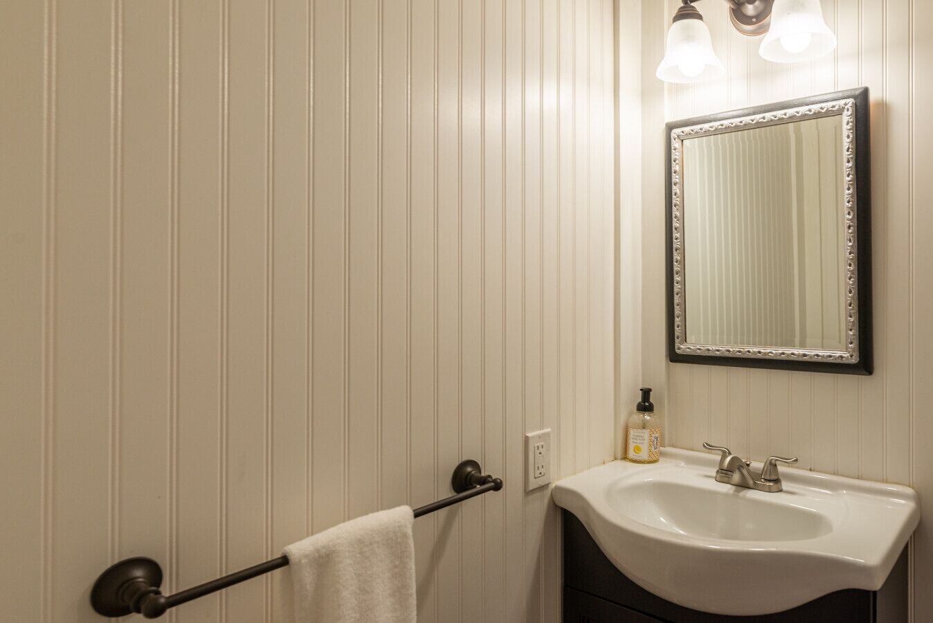 A bathroom with a white sink, a mirror with a decorative frame, and a towel rack with a white towel.