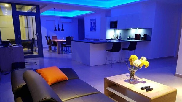 A modern living room with a sofa, a coffee table, and a kitchen in the background. - Suncity Luxury 2 bedroom apartment | Rooftop pool & Gym (Accra)