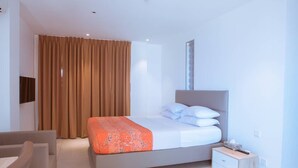 A modern hotel room with a bed, a bedside table, a chair, and a large window with curtains. - Suncity Luxury 2 bedroom apartment | Rooftop pool & Gym (Accra)