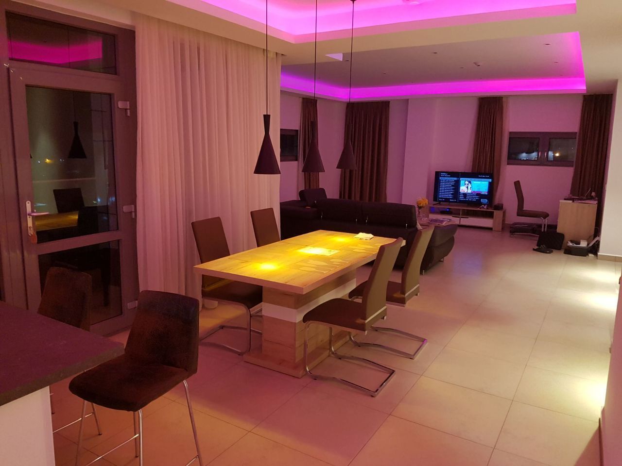 A modern dining area with a wooden table and chairs, a television, and a bar area.