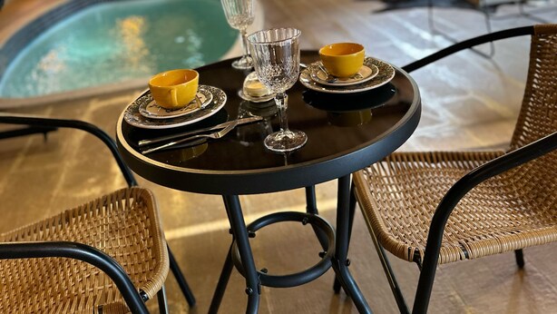 An outdoor pool area with a table set for two, surrounded by wicker chairs. - Pousada Dulce Ville (Domingos Martins)