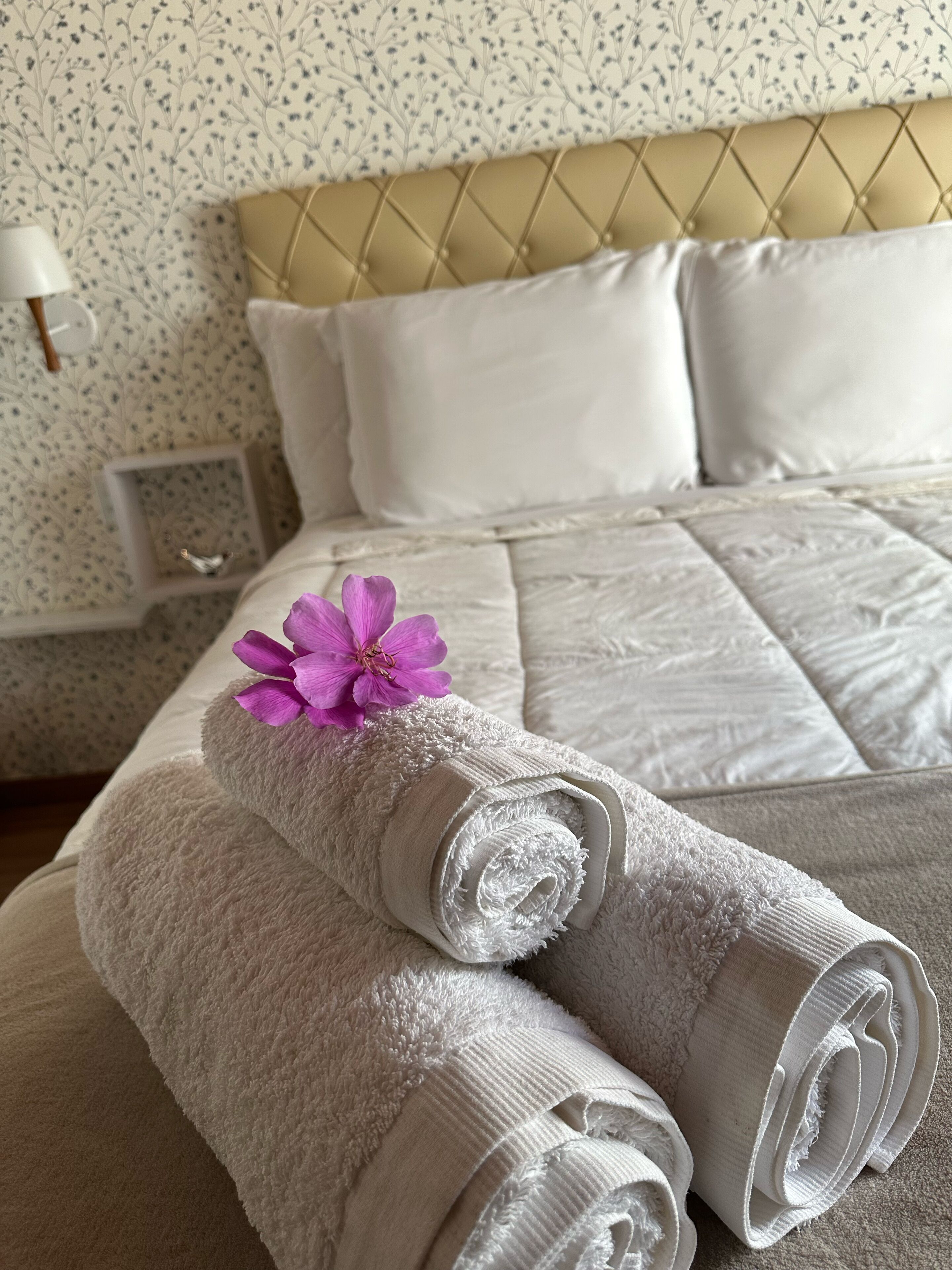 A neatly made bed with white linens and a purple flower on top.