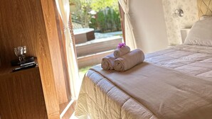 A bedroom with a wooden ceiling, a chandelier, a bed with a white duvet, and a view of greenery outside. - Pousada Dulce Ville (Domingos Martins)