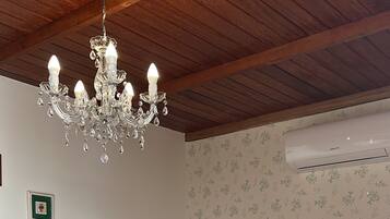 A bedroom with a wooden ceiling, a chandelier, a bed with a beige headboard, and an air conditioning unit on the wall.