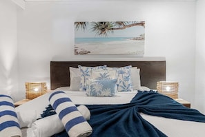 Une chambre à coucher avec un lit, des oreillers, une couverture, un tableau accroché au mur et des lampes de chevet.