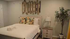 A bedroom with a wooden bed, a nightstand with drawers, a lamp, and a potted plant. - Fenced Backyard + Parking - Near Six Flags + AT&T (Forest Hill)