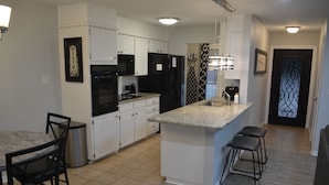 A modern kitchen with white cabinetry, a granite countertop, and a black refrigerator. There are two bar stools and a trash can. - Fenced Backyard + Parking - Near Six Flags + AT&T (Forest Hill)
