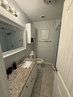 Bany amb taulell de granat, un lavabo blanc, vàter, dutxa amb envàs de vidre i un armari amb mirall.