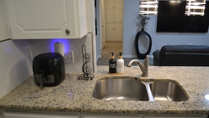 A kitchen with a granite countertop, stainless steel sink, white cabinets, a coffee maker, and two soap dispensers. - Fenced Backyard + Parking - Near Six Flags + AT&T (Forest Hill)