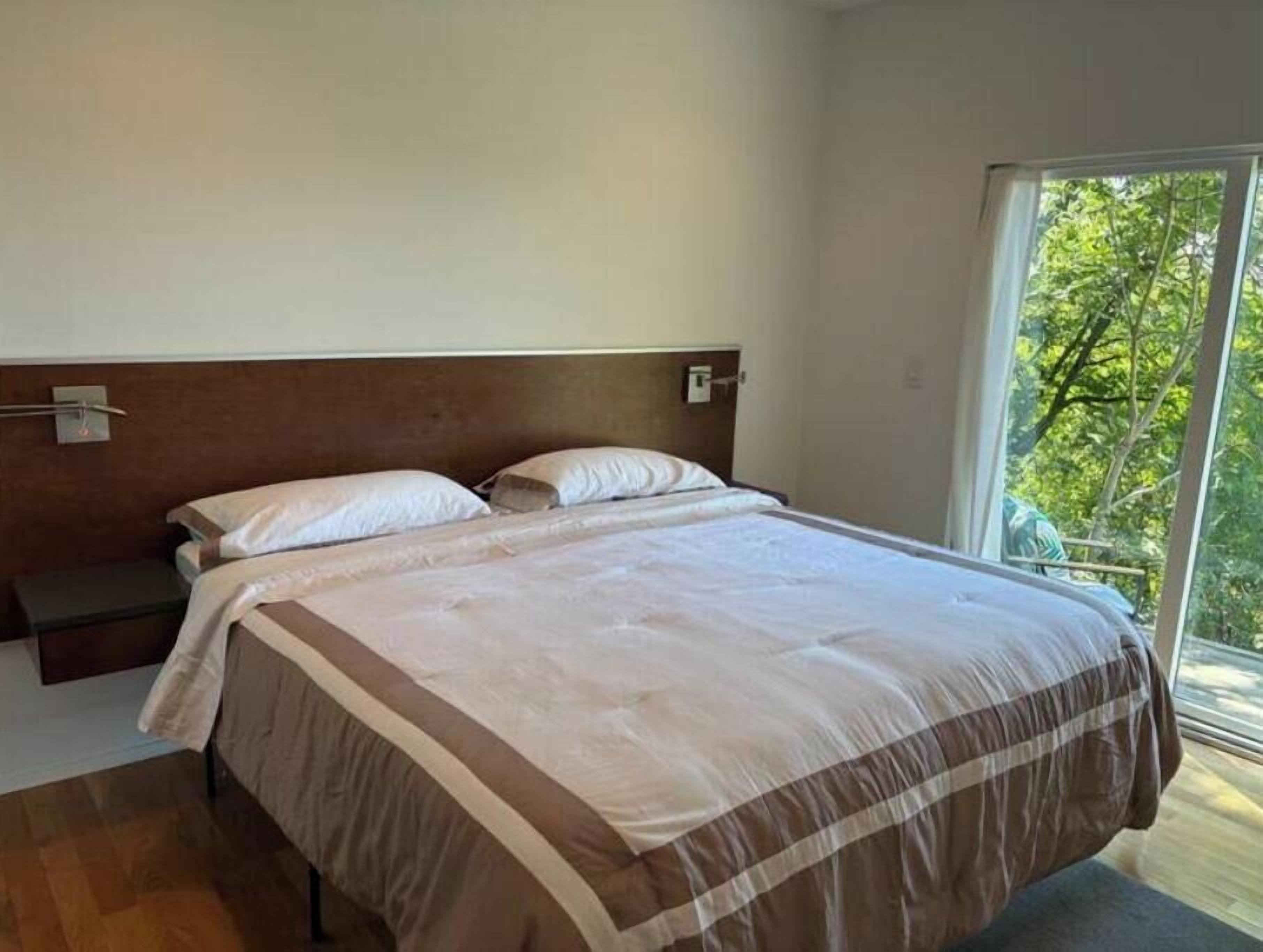 Una camera da letto con un letto grande, un comodino e una finestra vista alberi.