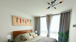 A bedroom with a bed, bedside table, lamp, curtains, a window, and a ceiling light fixture. - Vicuña Urban Stay (Santiago)