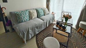A living room with a grey sofa, patterned cushions, a coffee table with bowls, a small stool, and a round rug. - Vicuña Urban Stay (Santiago)