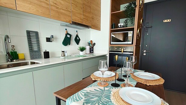 A modern kitchen with wooden cabinets, a dining table set with plates and glasses, and a small island with a plant. - Vicuña Urban Stay (Santiago)