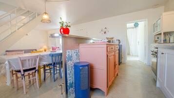 Une cuisine chaleureuse avec un coin repas, comprenant un escalier, une poubelle et un vase en forme de cœur posé sur le comptoir.