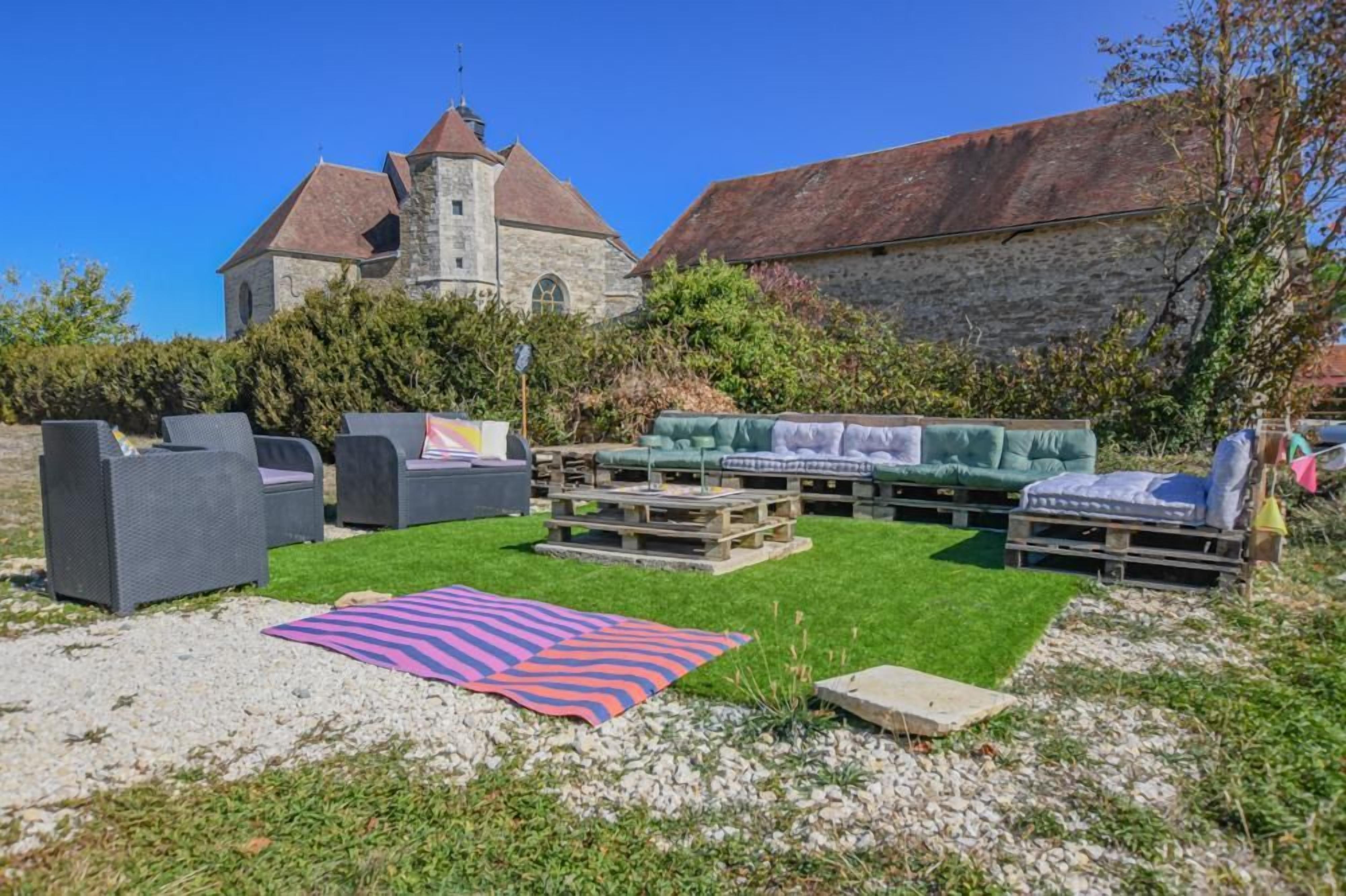 Ein Außenbereich mit Sofas und einem Tisch, ein Steinhaus mit einem Turm im Hintergrund und eine Rasenfläche.