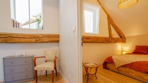Een slaapkamer met een houten plafond, een bed met rode beddengoed, een stoel, een klein tafeltje en een dressoir.