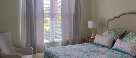 A bedroom with a bed, a chair, a nightstand with a lamp, and a ceiling fan.