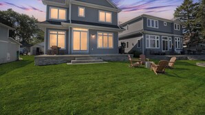 Ein zweist öckiges Haus mit gepflegtem Rasen und einer Sitzgelegenheit im Freien.