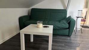 Una habitación con piso de madera oscura, una mesa blanca con un candelabro de vidrio y un sofá verde.
