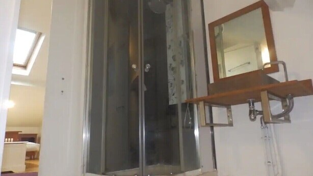Ducha de esquina con mampara de vidrio, repisa de madera con espejo arriba y lavamanos a la vista.