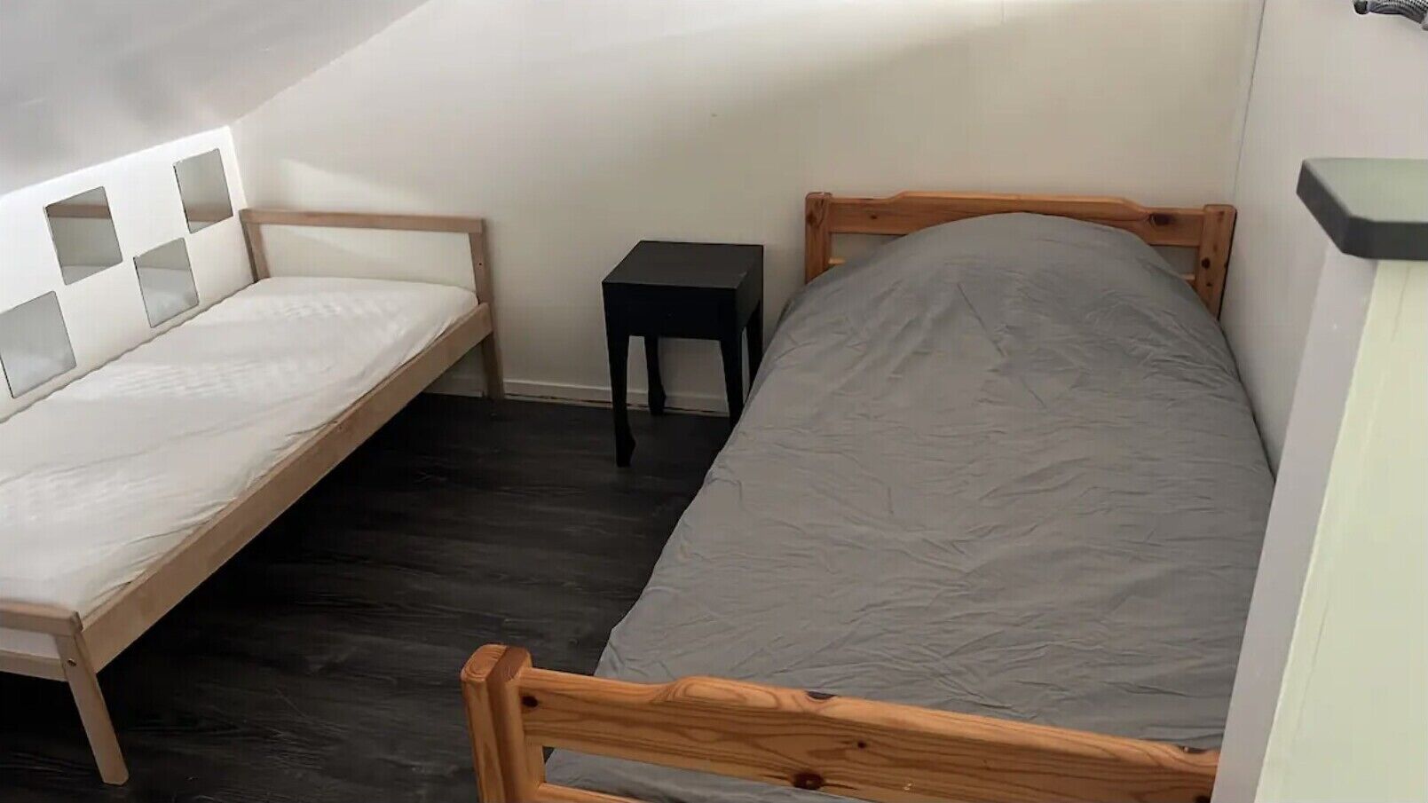 Una habitación pequeña con cama individual, techo inclinado y suelo de madera oscura.
